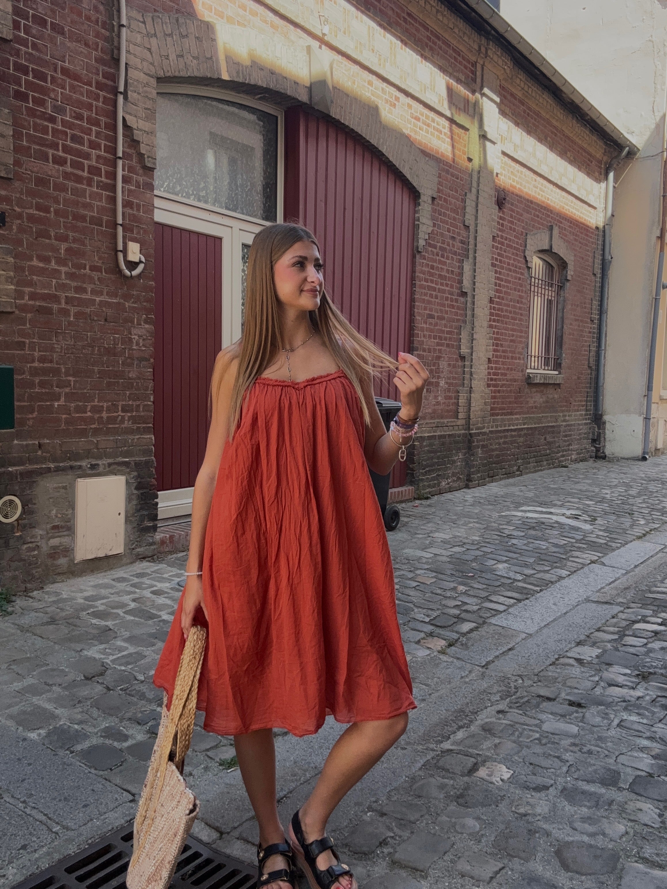 Robe courte terracotta à bretelles spaghetti portée dans une ruelle pavée