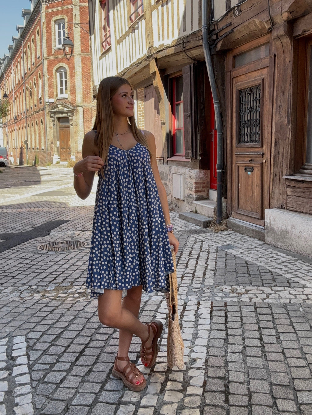 Robe courte bleu marine à pois blancs portée avec un panier en osier dans une ruelle pavée