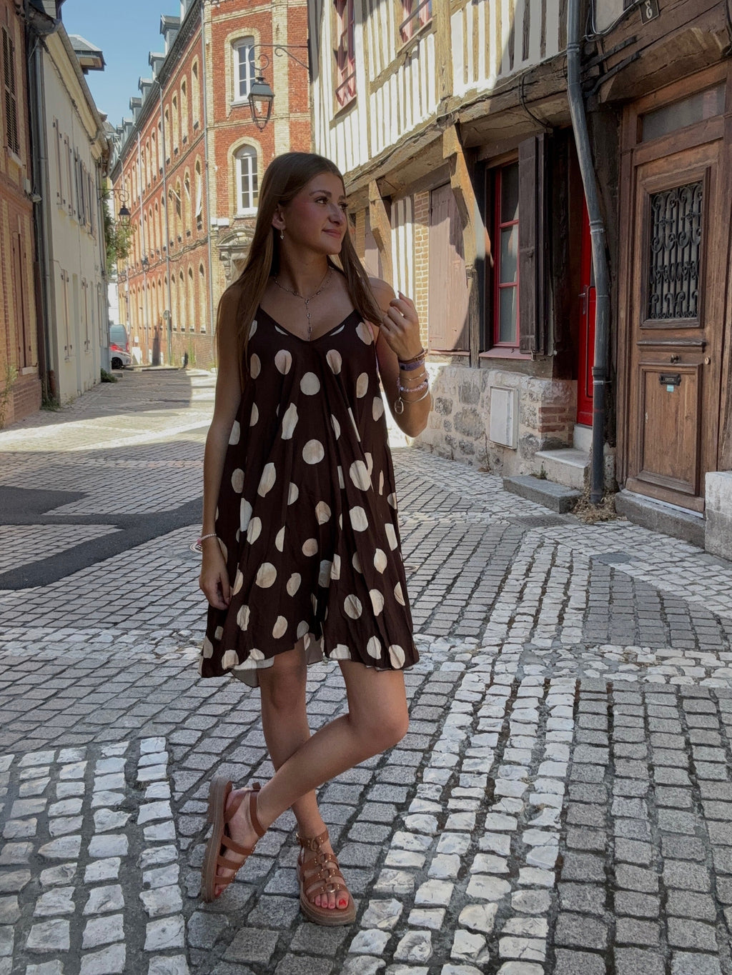 Robe courte chocolat à grands pois crème portée dans une ruelle pavée