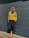 Pull col V jaune moutarde porté avec pantalon noir et sneakers