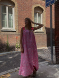 Robe longue rayée jaune et rose portée devant un mur de verdure