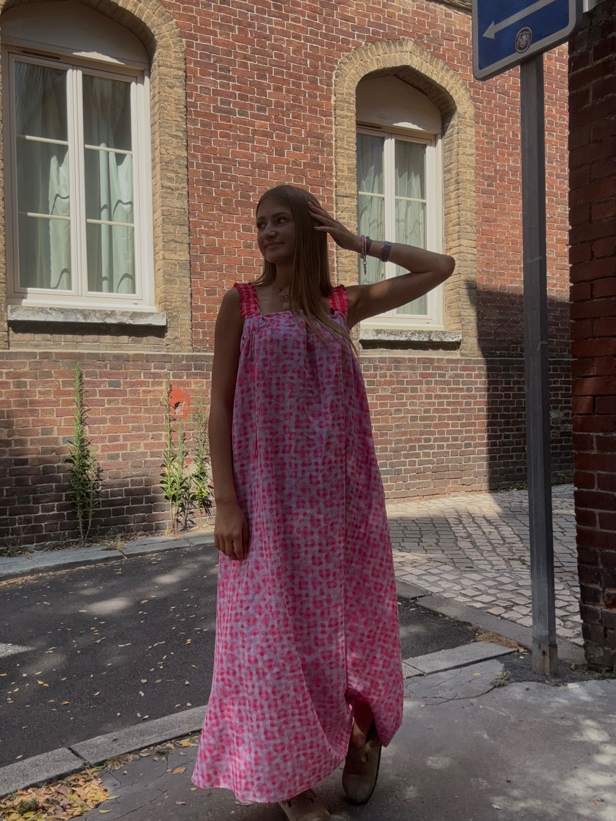 Robe longue rayée jaune et rose portée devant un mur de verdure